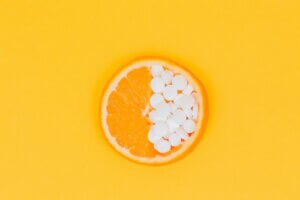 Half orange half vitamin C pills on orange background for article supplements to decrease inflammation in the body